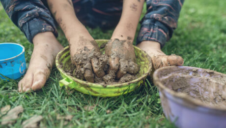 Toddler child enjoying nature playing with mud